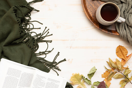 Border of open bible, autumn leaves, cup of coffee and green blanket on a white wood background with copy space