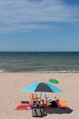 Fototapeta na wymiar Langrune-Sur-Mer, France - 08 04 2022: Two women lying under an umbrella on the beach and reading