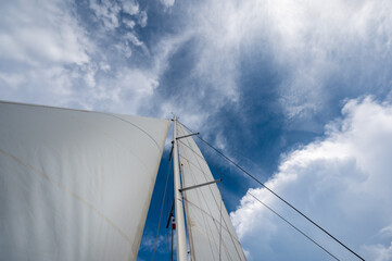 Fototapeta premium Looking up at white sails on a sail boat with blue skies and partly cloudy conditions