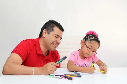 Latino dad and daughter, teacher and student draw in a notebook with colors in this back to school to improve skills with Autism Spectrum Disorder (ASD)