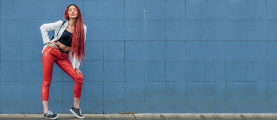 redhead funky urban hipster girl posing on the street isolated on blue wall background