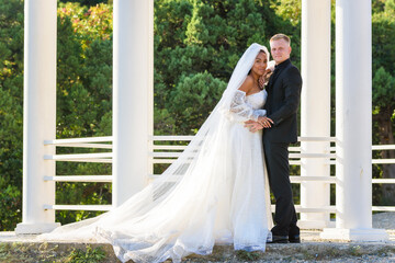Fototapeta premium Portrait of a mixed race newlyweds in front of a gazebo with round columns