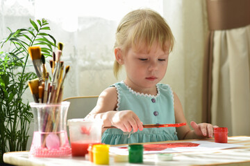 A two-year-old girl is sitting at a table and drawing with gouache. Development of fine motor...