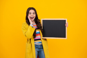 Fototapeta na wymiar Teenage girl child holding blackboard, isolated on a yellow background. Amazed teenager. Excited teen girl.
