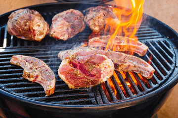 Raw traditional barbecue lamb shanks and saddle grilled as close-up on a charcoal grill with fire and smoke