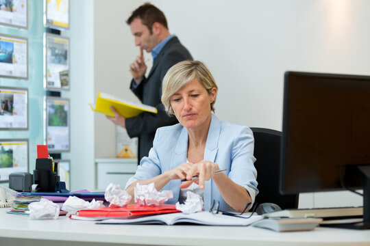 Woman At Office Desk Surrounded By Screwed Up Paper