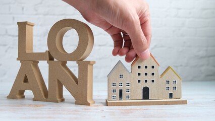 左寄りのローンの文字を木製背景にセットして家を手で置いた写真