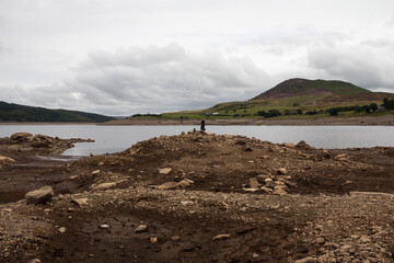 Reservoir in Wales illustrating why rationing and hosepipe bans are required as man stands at edge...