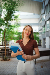Portrait of student girl looking at camera and holding notebooks while she is at university campus