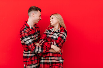 Happy Saint Valentine's Day. Smiling young couple in the same pyjamas having fun on red background....