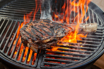 Barbecue dry aged wagyu tomahawk steak offered as close-up on a charcoal grill with fire and smoke