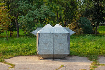 Large clean trash can in the park against the background of trees and grass