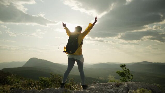 A girl on top of a mountain raises her hands up, a feeling of freedom and happiness. Woman hiking in the mountains, tourist trip in landscape nature. High quality 4k footage