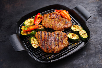 Traditional barbecue pork neck steak with grilled vegetable and spices served as close-up in a rustic design frying pan
