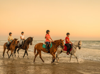 3 young women and a man riding their horses by the sea