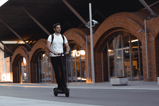 Attractive Young Man Riding Modern Kick Scooter At Cityscape Background.