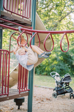 5 year-old Caucasian, blonde boy hangs from monkey bars at playground.