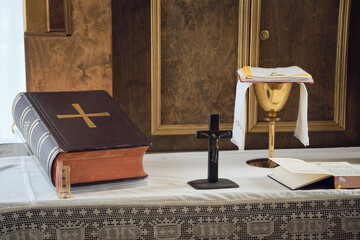 Catholic symbols composition. The Bible, wooden cross and golden chalice on the altar.