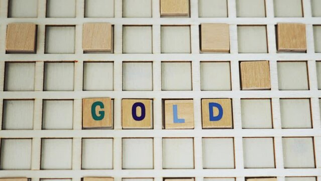 Short closeup clip showing a palm of an unrecognizable caucasian person putting wooden letters together creating the word GOLD. Wordplay concept. High quality 4k footage