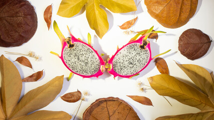 AUTUMN, DRAGON FRUIT, PITAHAYA WITH RED SKIN AND WHITE PULP ON WHITE BACKGROUND WITH DRY LEAVES