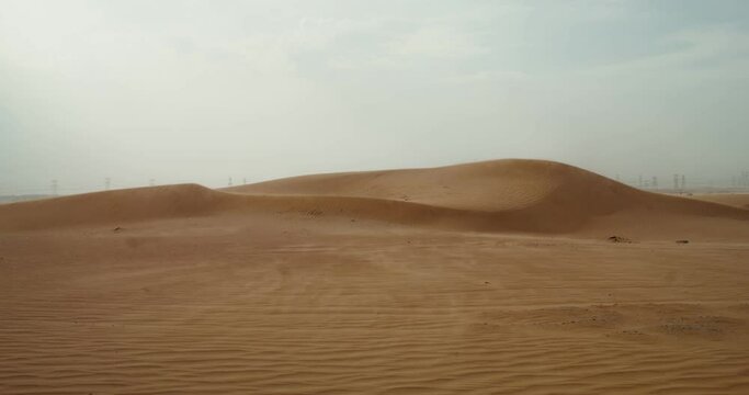 The wind inflates the sands of the desert, forming a beautiful sandy pattern. Desert sand dunes. Power lines in the background. 4k video, red komodo