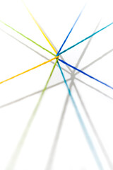 Yellow, green, blue, teal, yarn intertwined and radiating outward casting shadows on a white...