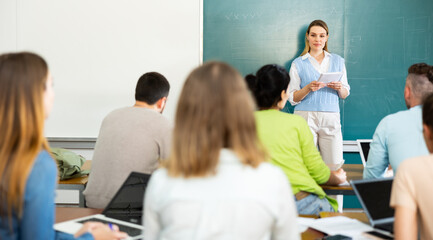 Group of students attentively listening to lecture of female teacher in classroom