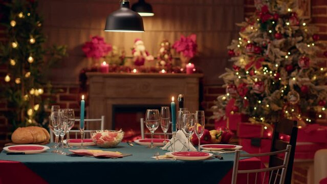 Empty traditional Christmas dinner table inside decorated living room with holiday garlands and dinnerware. Interior of traditional and authentic season cozy setting celebrating religious event.