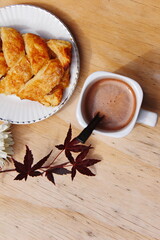 Coffee mugs and pastries served on a wooden table with crimson Japanese maple leaves and white daisies. Top view photo.