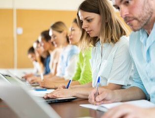 Fototapeta premium Woman university student sitting at table in classroom and writing.