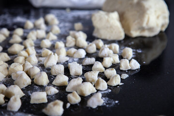 Homemade gnocchi preparation, small pieces of cut dough on black table with flour. Focus on small pieces of cut dough.