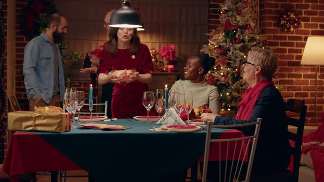 Senior conversating with young man about rare bottle of champagne brought at Christmas dinner table. Chherful diverse women sitting in living room while celebrating winter traditional holiday