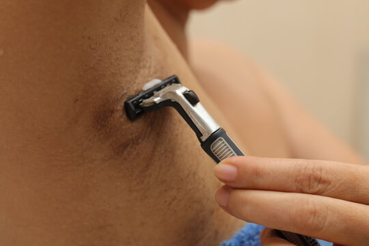 Female unshaved armpits or woman with long hair underarm, depilation, hair removal concept. Young woman shaves hairy armpits with a disposable razor. Close-up, selective focus.