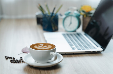 Art latte hot coffee cup on wooden table at the office.