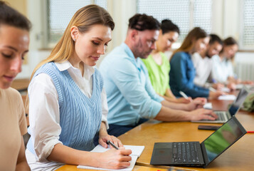 Fototapeta premium Woman university student sitting at table in classroom and writing.