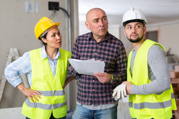 Interested adult male homeowner discussing home renovation work plan with builders while standing...