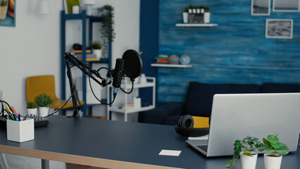 Empty living room studio desk with modern laptop and professional podcast microphone. Social media workstation equipped with digital content creator tools and devices with nobody in it.
