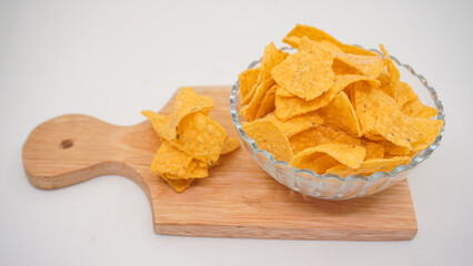 Selicious nachos chips in glass bowl on a cutting board, isolated on white background