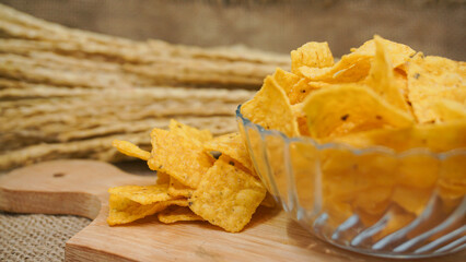 Selicious nachos chips in glass bowl on a cutting board, isolated on burlap background