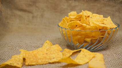 Selicious nachos chips in glass bowl on a cutting board, isolated on burlap background