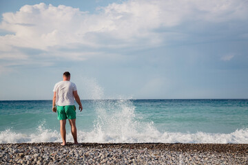 attractive young adult man stands with his back on the shore of the mediterranean sea with waves. copy space