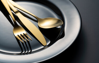 Gold knives, forks and spoons on black plates.