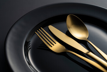 Gold knives, forks and spoons on black plates.