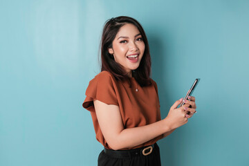 Naklejka premium A portrait of a happy Asian woman is smiling and holding his smartphone wearing brown shirt