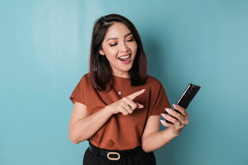 A portrait of a happy Asian woman is smiling and holding his smartphone wearing brown shirt