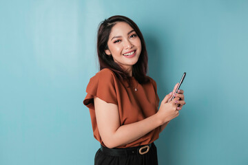 Naklejka premium A portrait of a happy Asian woman is smiling and holding his smartphone wearing brown shirt