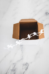 Think outside the box concept with paper people chain getting out of a white box on white marble