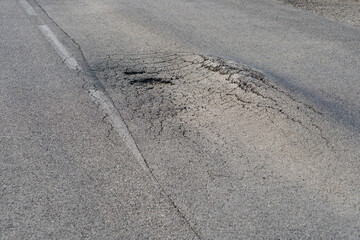 Broken road with holes and cracks built in countryside on hot sunny day. Deformed and expanded asphalt surface with potholes caused by heavy overloaded trucks driving on highway at rural site closeup