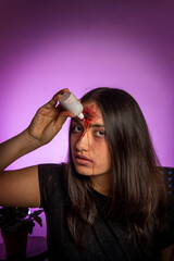 Woman looking at camera while characterized by horror makeup for halloween knowing drops of fake...