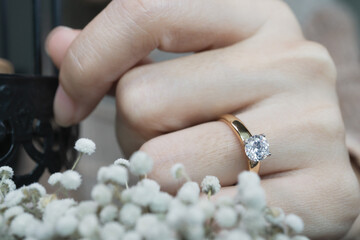 Close up of an elegant diamond ring on woman finger while touching white flower with sunlight and shadow background. love and wedding concept. Soft and selective focus.